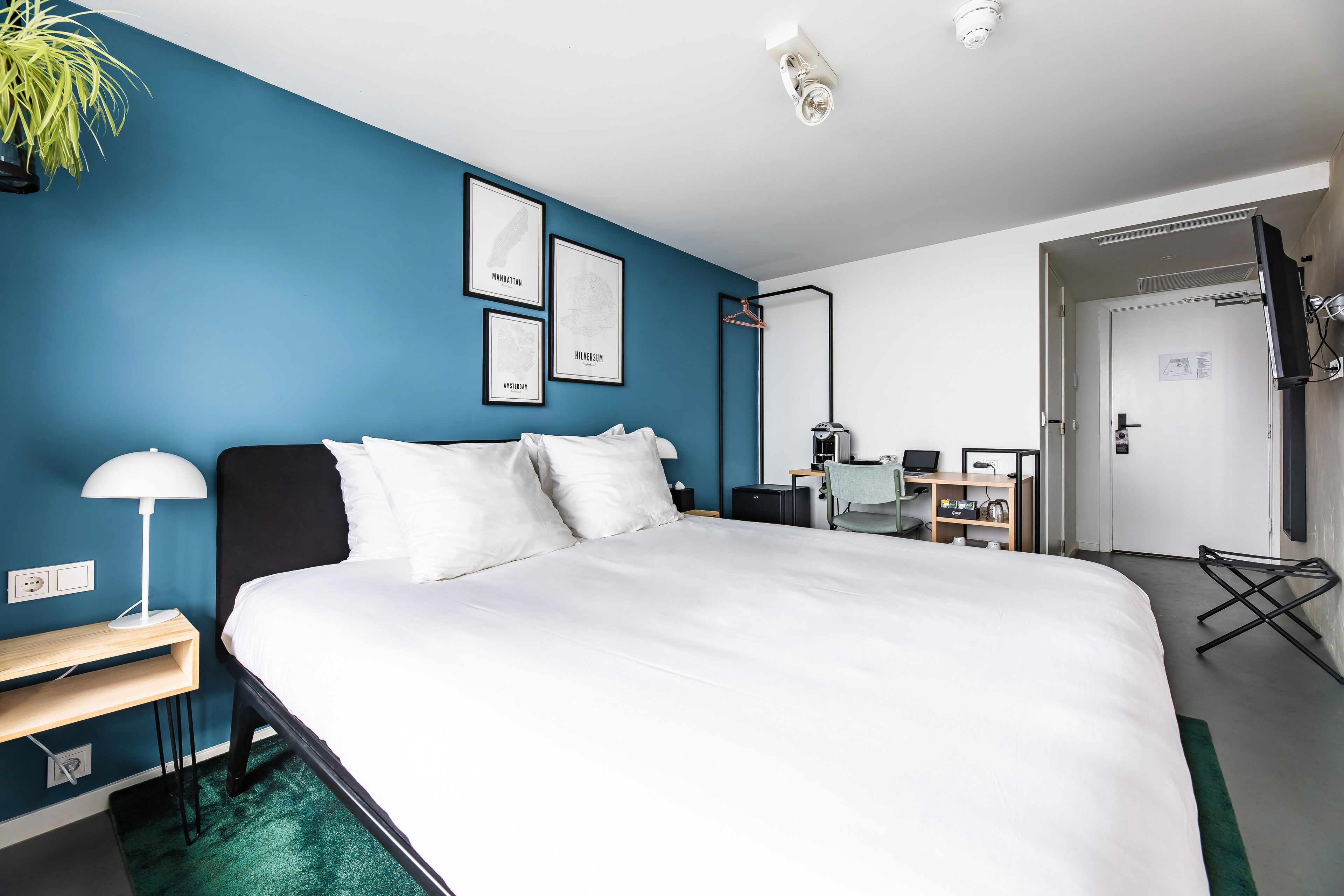 A modern hotel room with a large bed, a desk, a chair, and a TV.