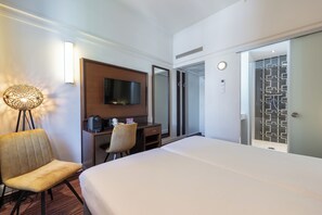 Une chambre d’hôtel comprenant un lit, un bureau avec une télévision, une chaise et une salle de bain avec douche.