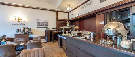A hotel dining area with a buffet setup, wooden flooring, and a view of the cityscape.