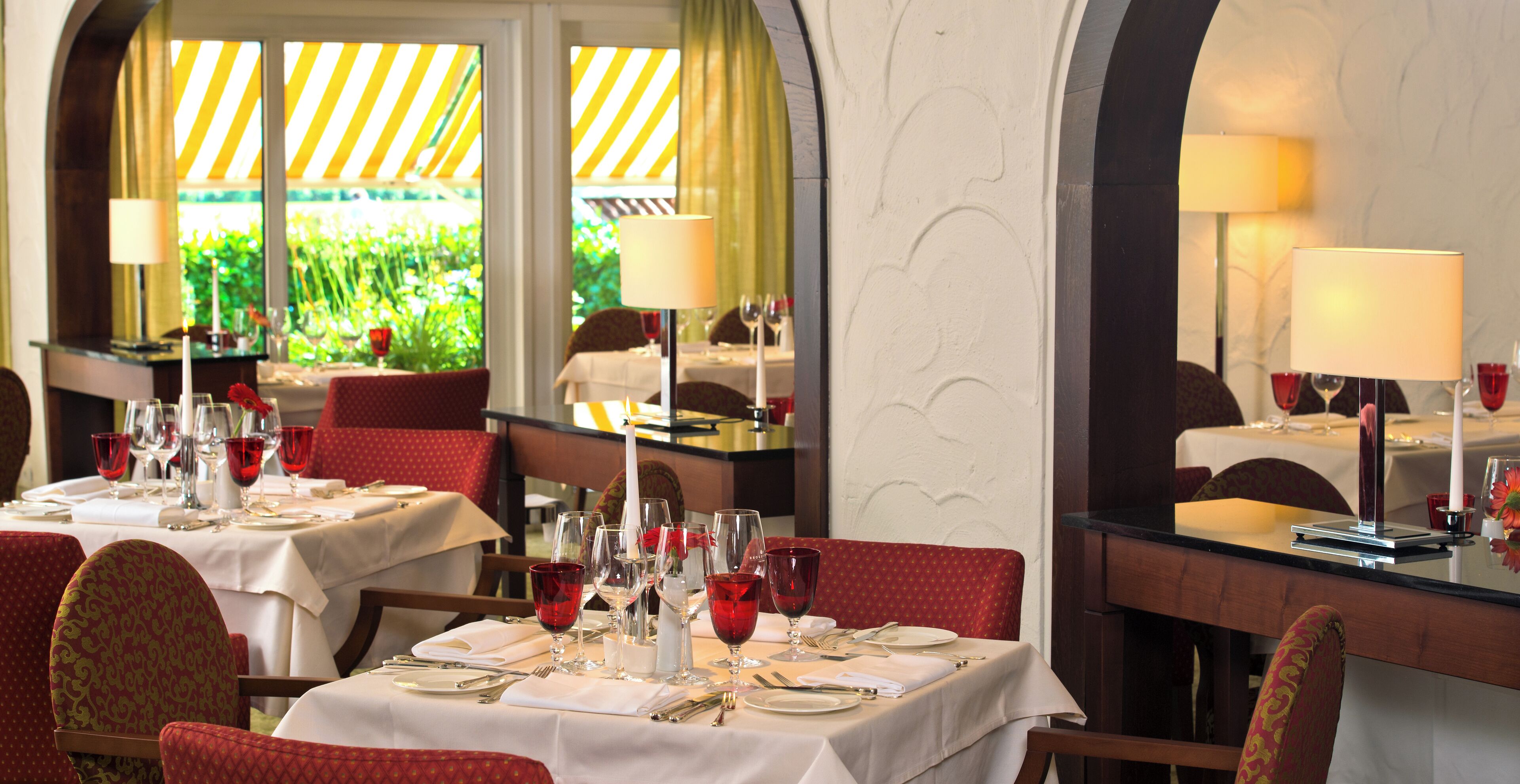 Un restaurante con mesas dispuestas para comer, con sillas rojas y manteles blancos.