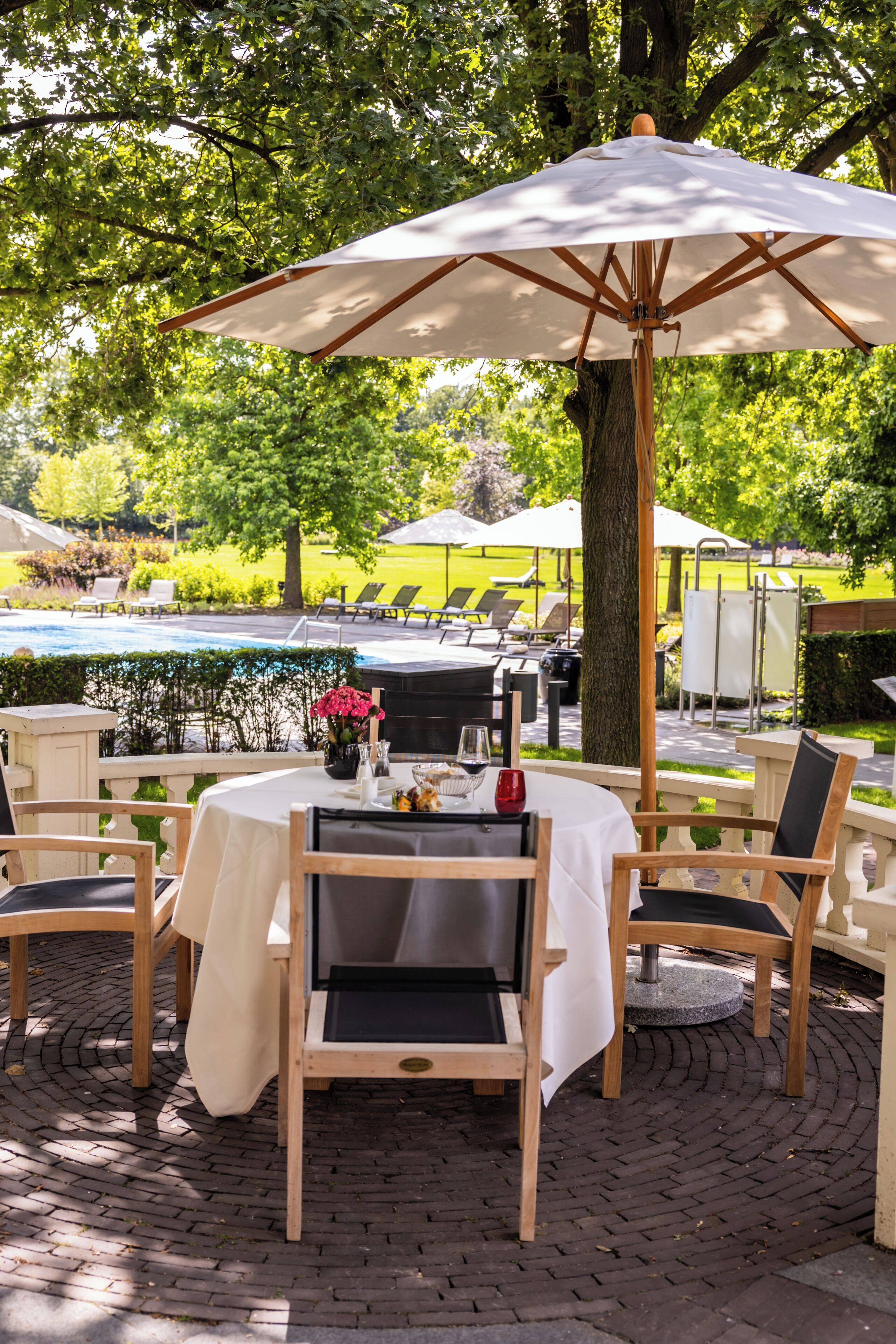 Un área de comedor al aire libre con una mesa lista para dos personas, rodeada de sillas y cubierta por una sombrilla grande.