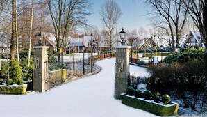 A snow-covered pathway leading to a gated entrance with a brick wall and a metal gate. - Fletcher Parkhotel De Wiemsel (Ootmarsum)