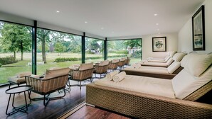 A sunlit room with wicker furniture, large windows, and a view of a garden. - Fletcher Parkhotel De Wiemsel (Ootmarsum)