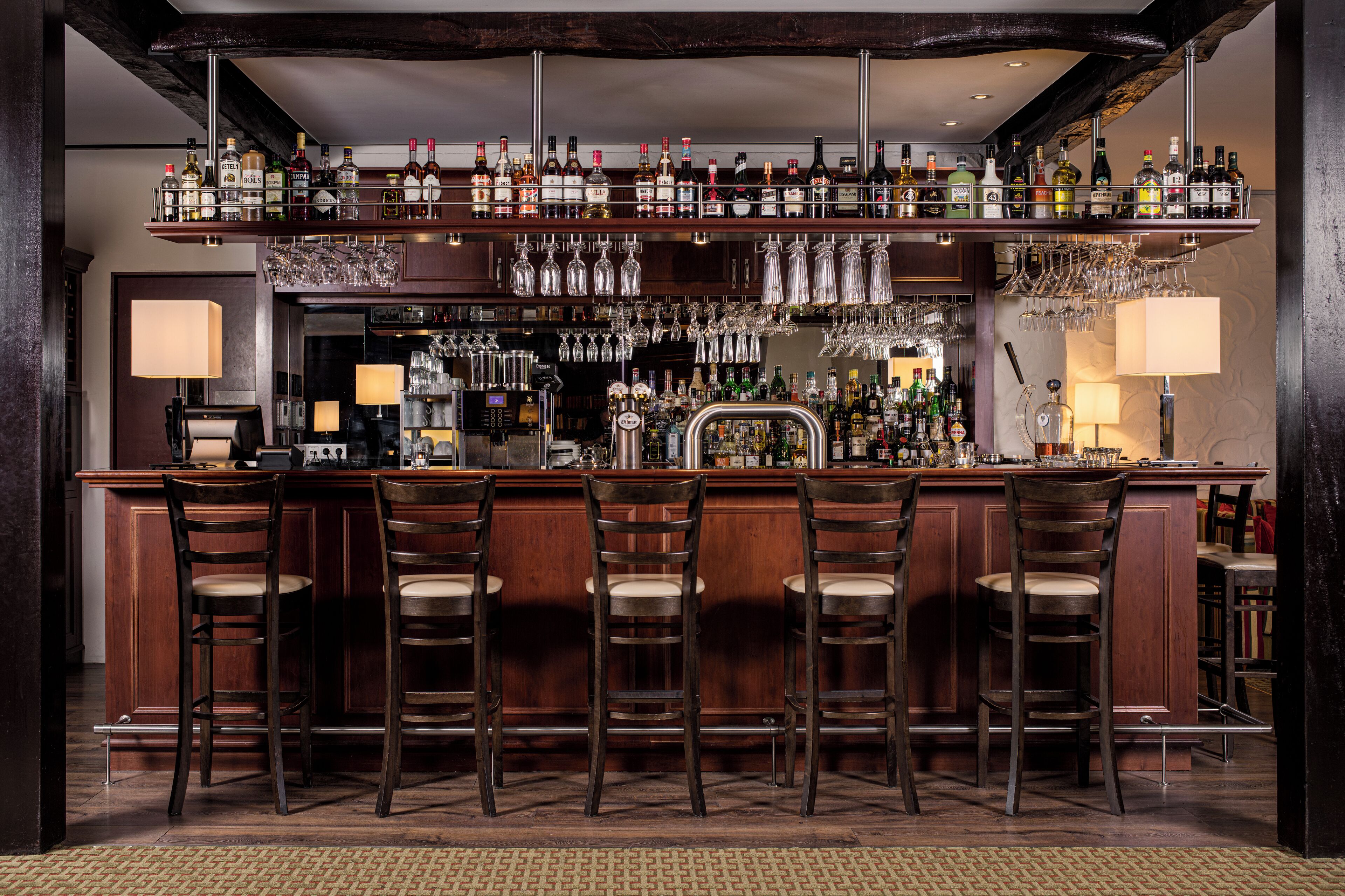 A bar area with multiple liquor bottles, glasses, and bar stools.