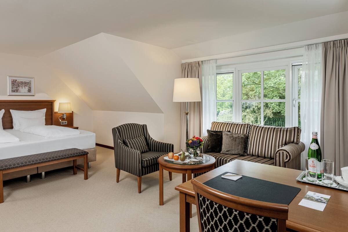Une chambre d’hôtel comprenant un lit, un canapé, une table à manger, un banc et une fenêtre avec des rideaux.