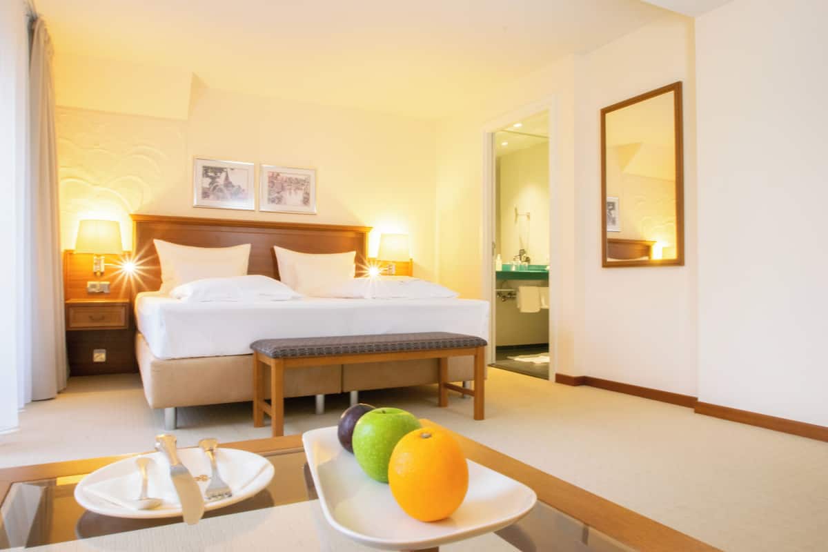Une chambre d’hôtel avec un lit, des lampes de chevet, une table de chevet sur laquelle se trouve une assiette de fruits, et un miroir au mur.