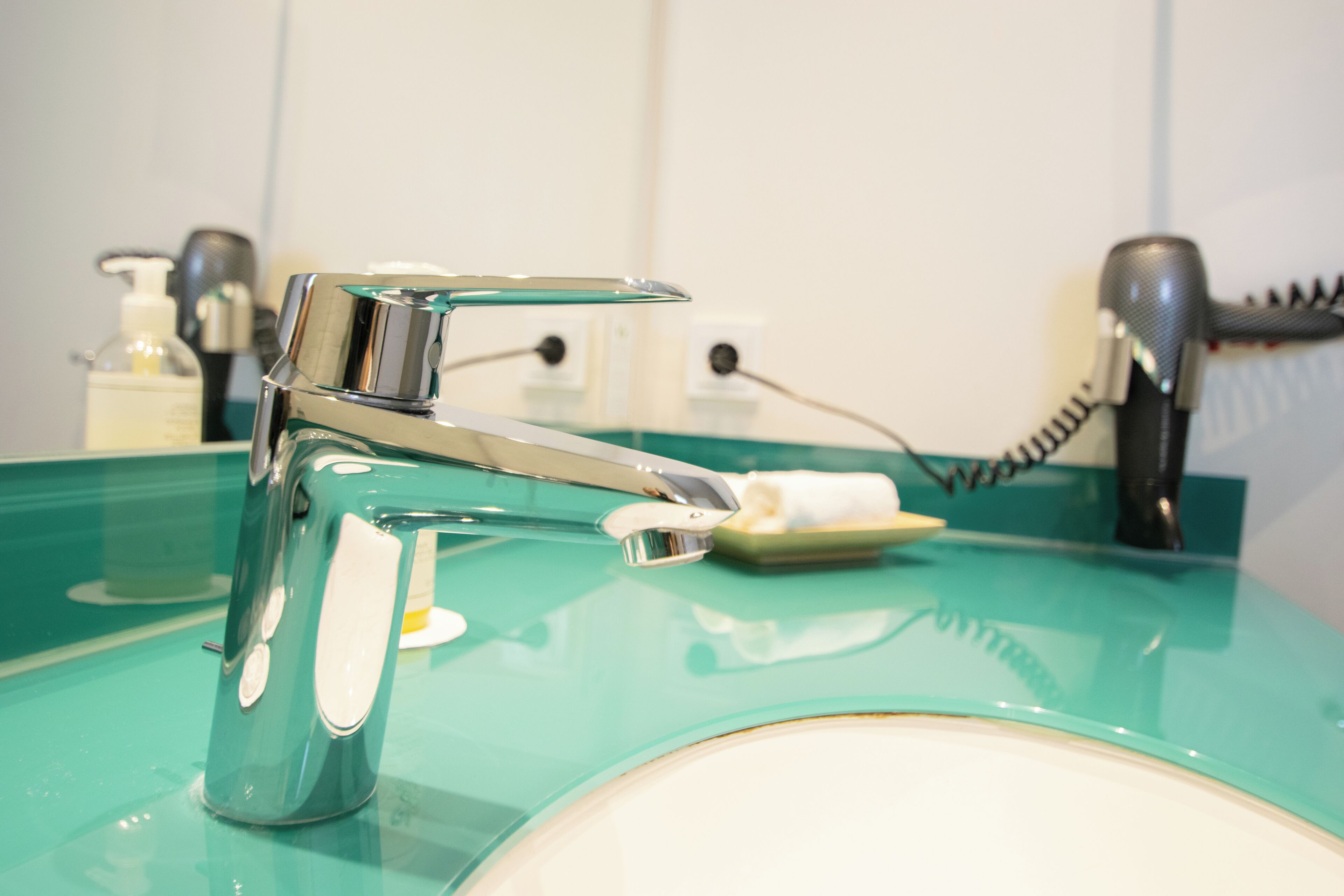 A modern bathroom with a chrome faucet, a green sink, and a hairdryer on the counter.
