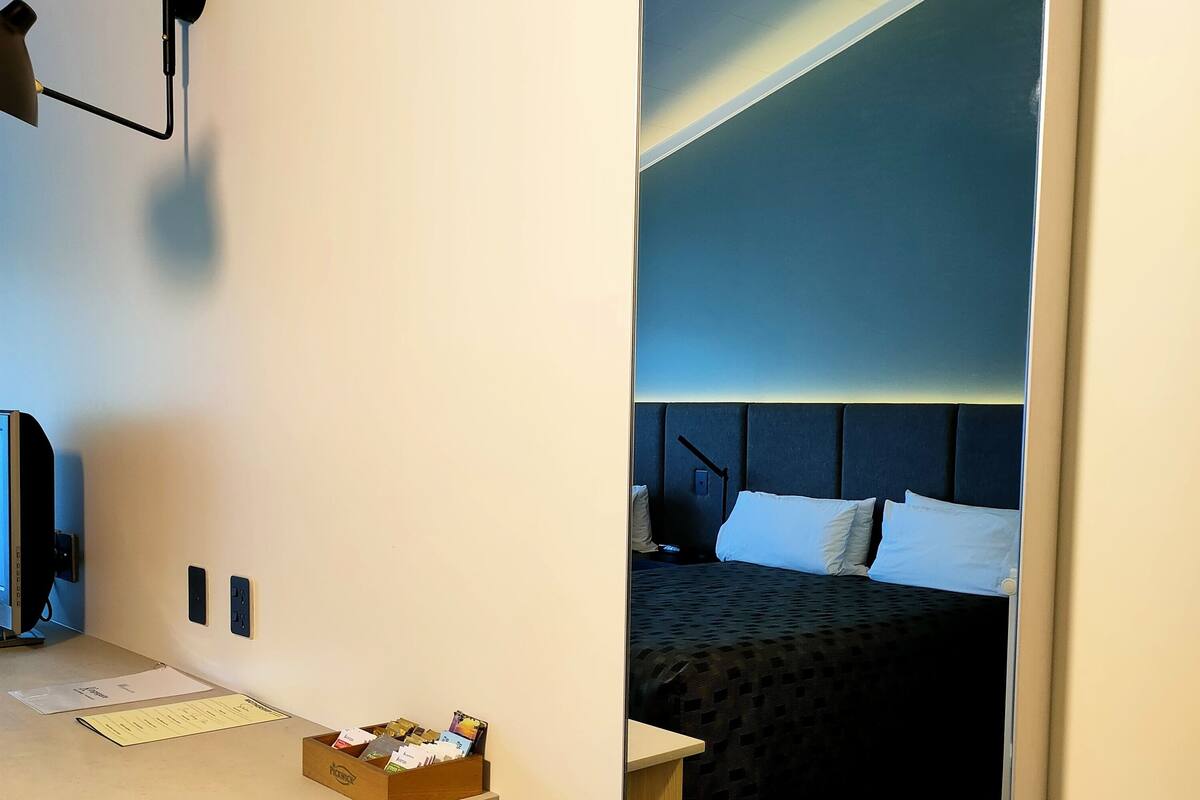 Een hotelkamer met een bed, een bureau, een bankje, een spiegel en een wandlamp.