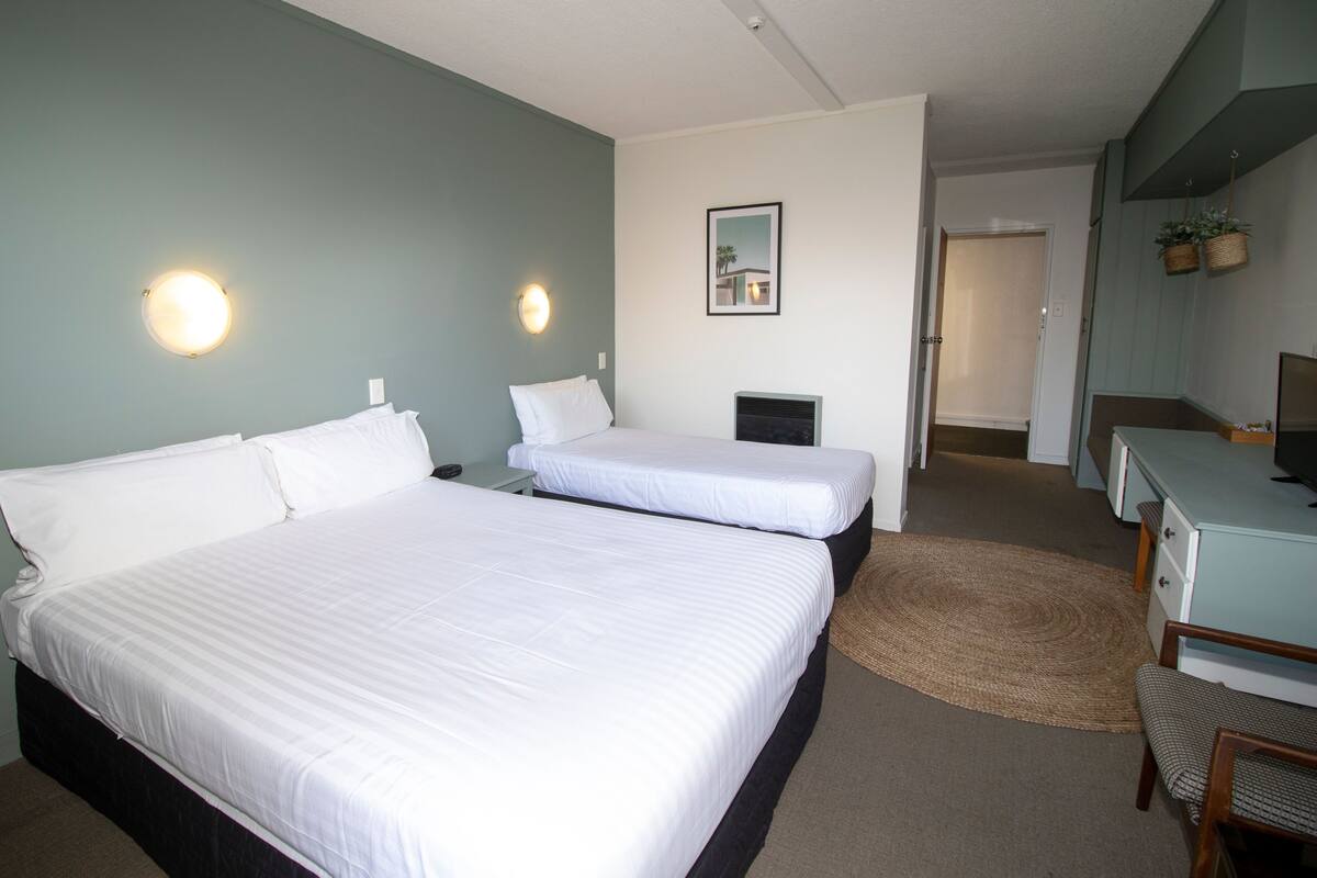 Een hotelkamer met twee bedden, een bureau, een stoel, een kleine televisie en een spiegel aan de muur.