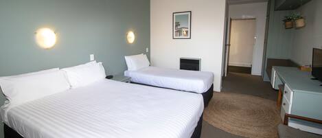 A hotel room with two beds, a desk, a chair, a small TV, and a mirror on the wall.