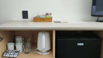 A compact kitchenette with a refrigerator, coffee maker, and storage shelves.