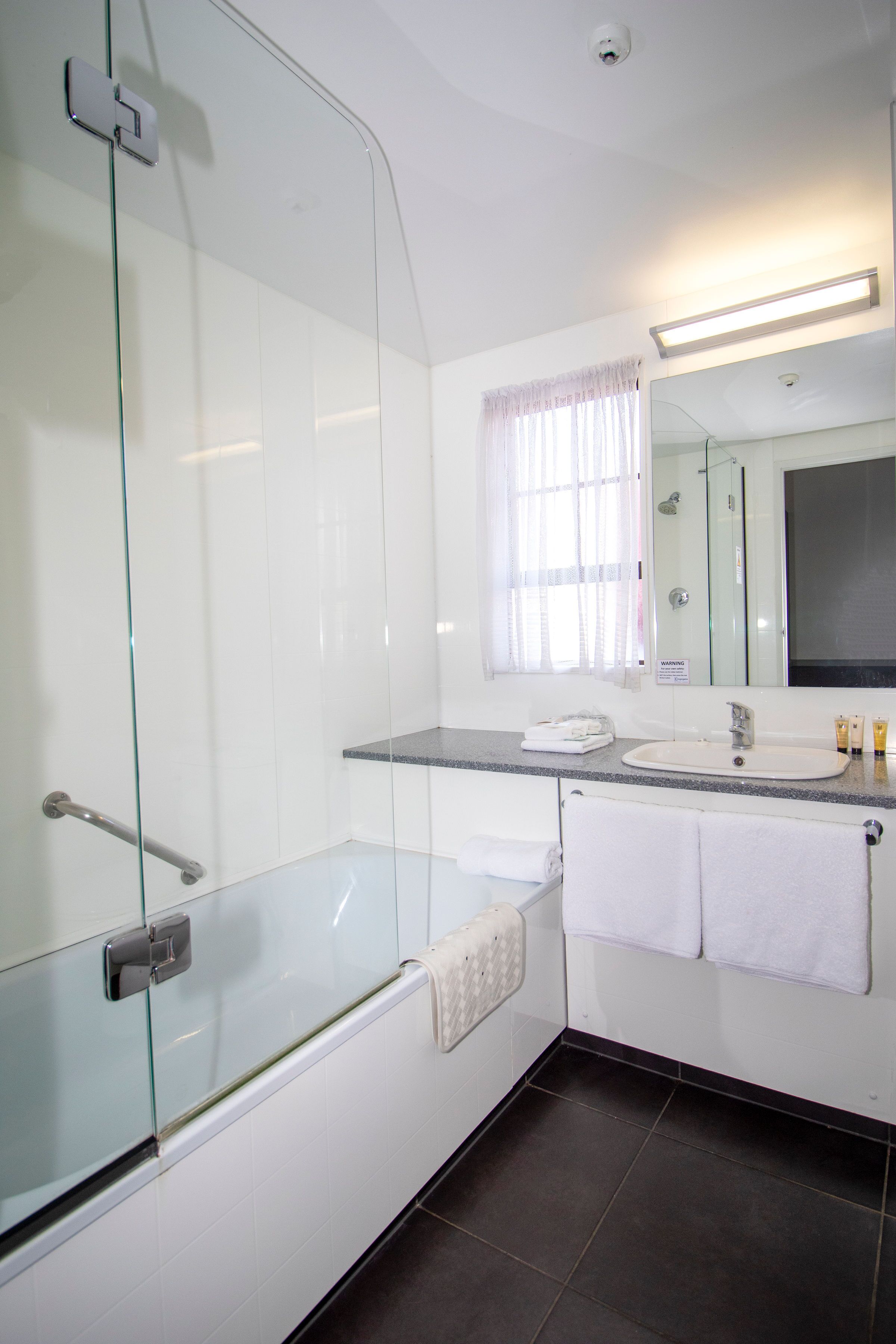 A modern bathroom with a glass-enclosed shower, a vanity with a sink and mirror, and a window with curtains.
