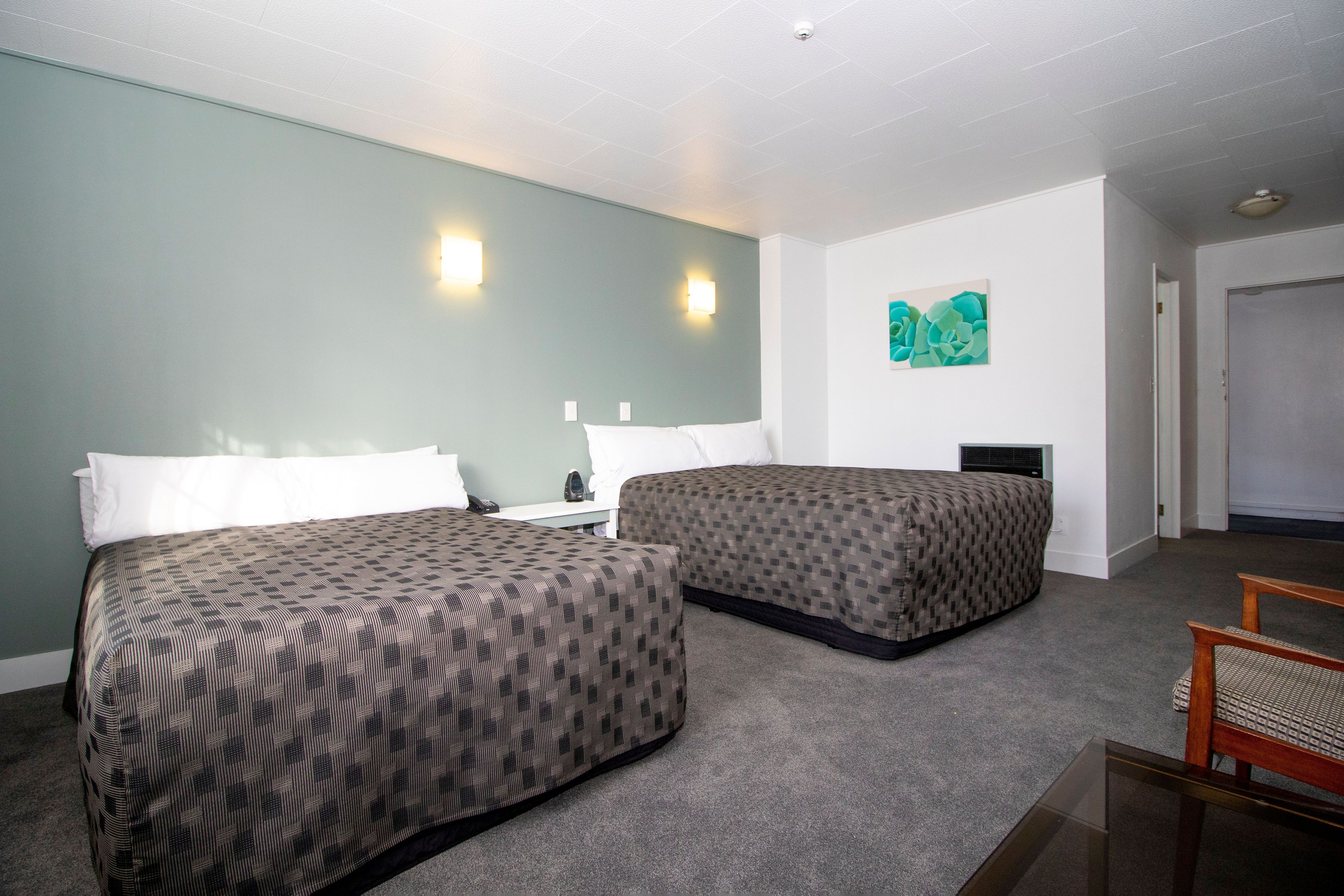 Une chambre d’hôtel avec deux lits, une petite table, une chaise et un tableau au mur.