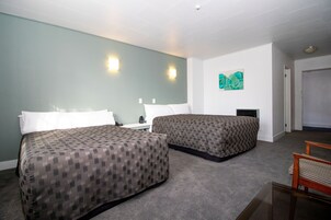 Habitación de hotel con dos camas, una mesita, una silla y un cuadro en la pared.