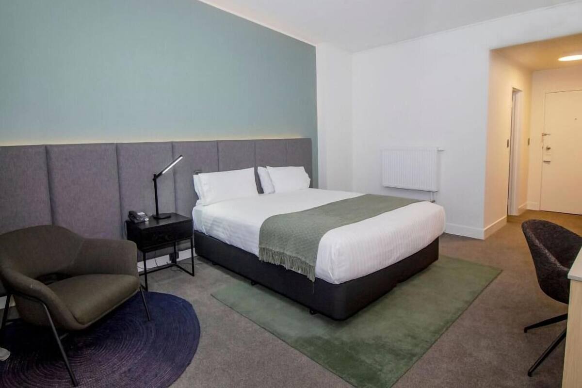 Een hotelkamer met een bed, een bureau, een stoel en een radiator.