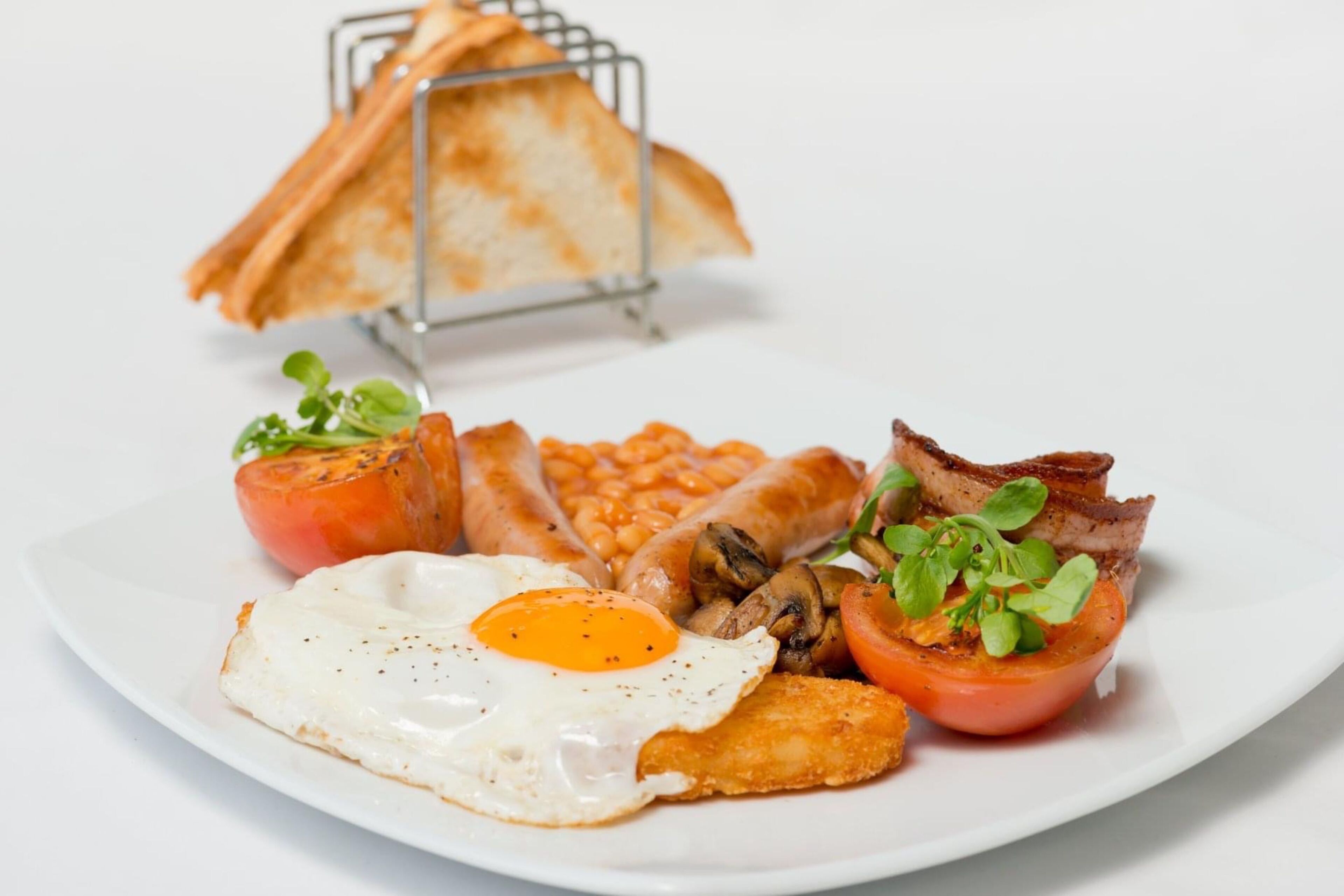 A plate of breakfast food including eggs, sausages, beans, mushrooms, bacon, and toast.