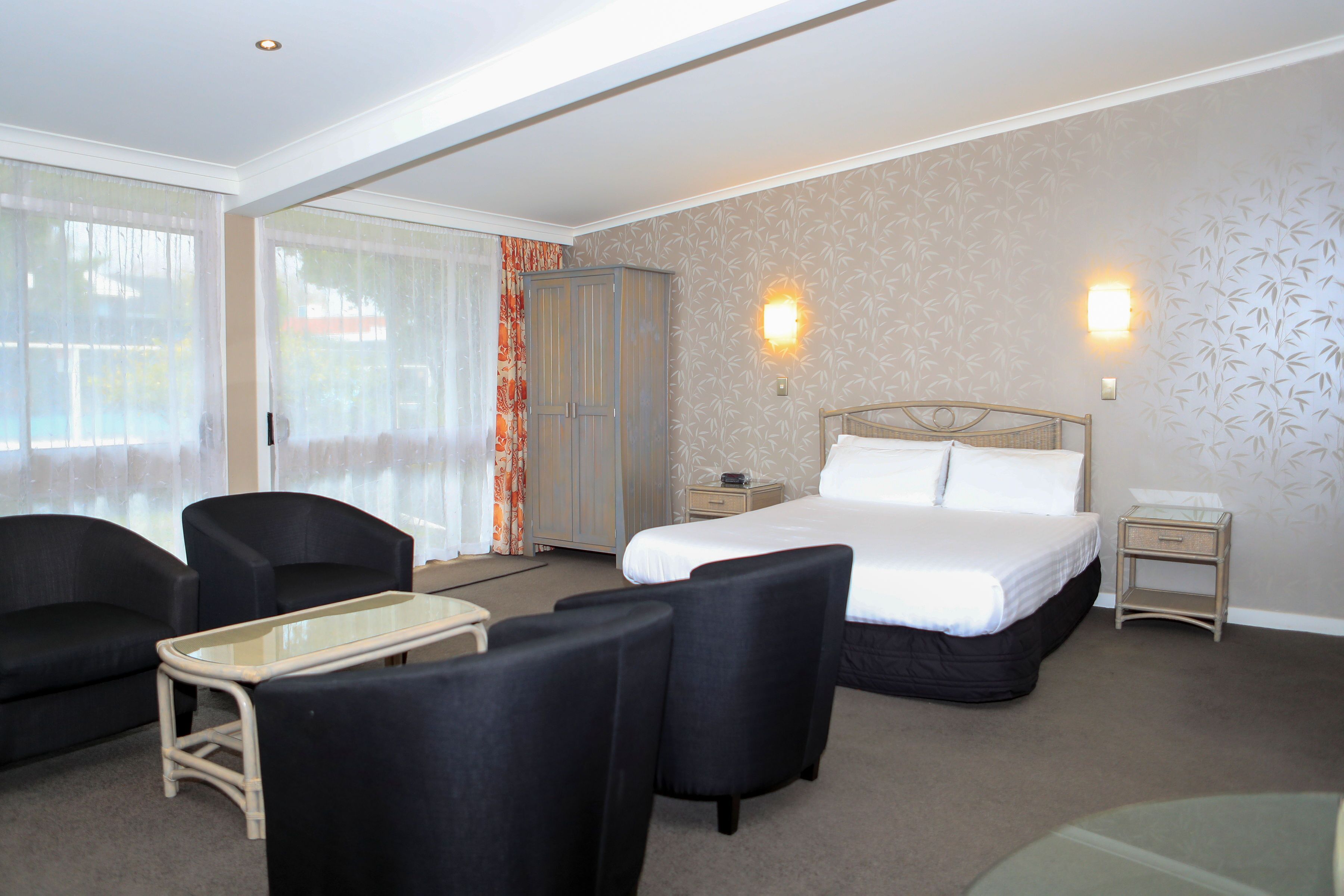 A hotel room with a bed, two bedside tables, a nightstand, a glass-top table, two armchairs, and a sofa.