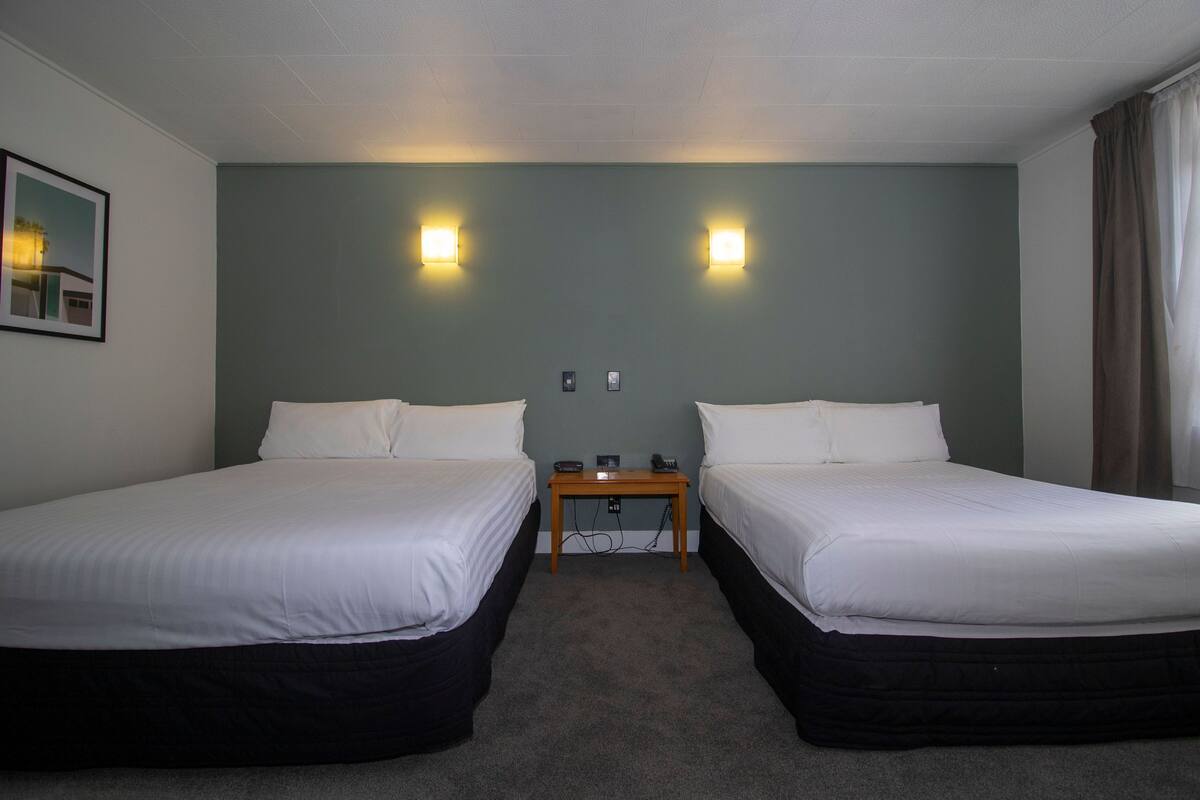 Een hotelkamer met twee eenpersoonsbedden, een klein tafeltje en twee wandlampen.