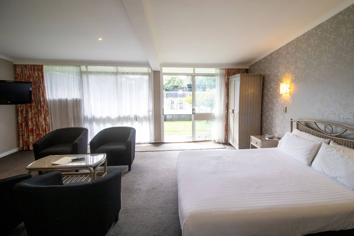 Hotelkamer met een groot bed, twee fauteuils, een tafeltje, een televisie en een glazen schuifdeur naar een buitenruimte.