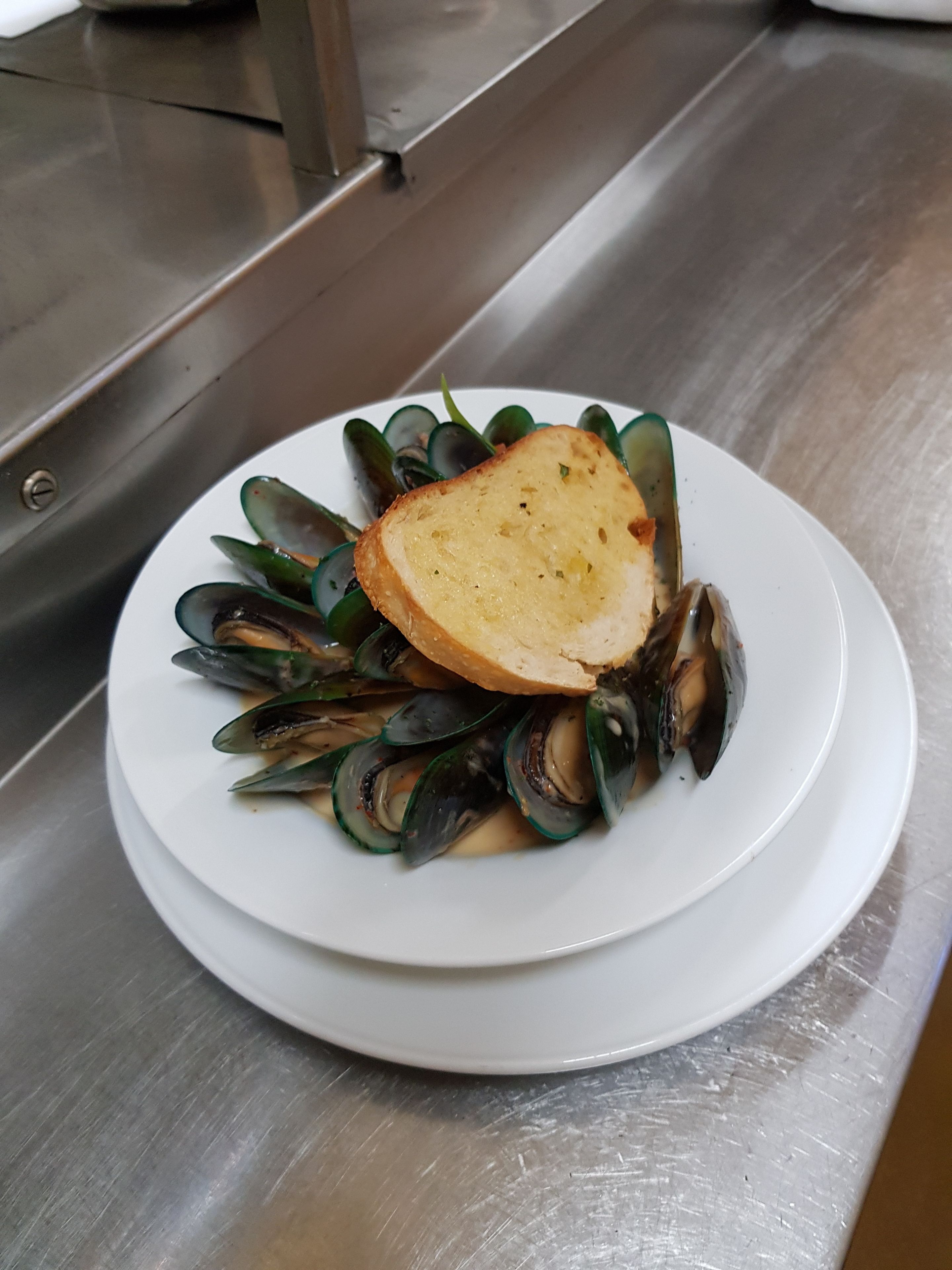 Une assiette de moules, accompagnée d’une tranche de pain, sur une assiette blanche.