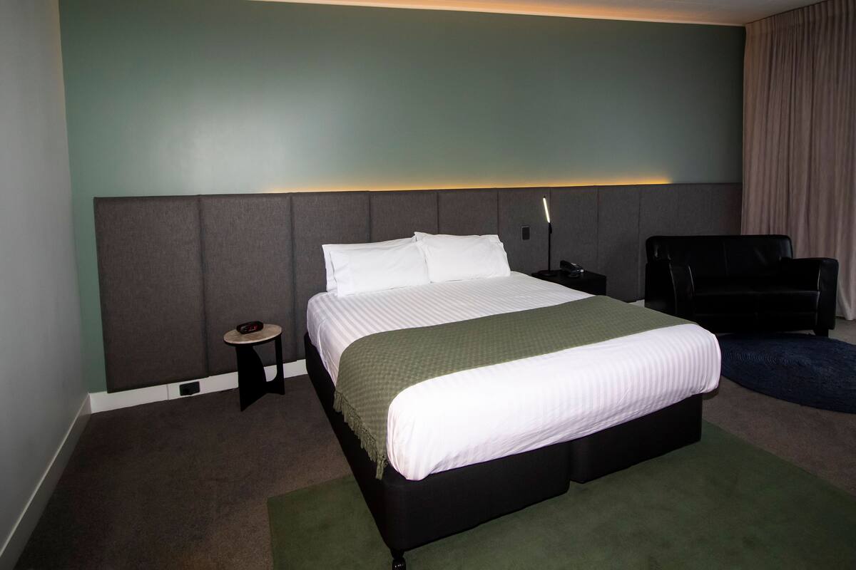 Een hotelkamer met een groot bed, een nachtkastje, een stoel en een lamp.