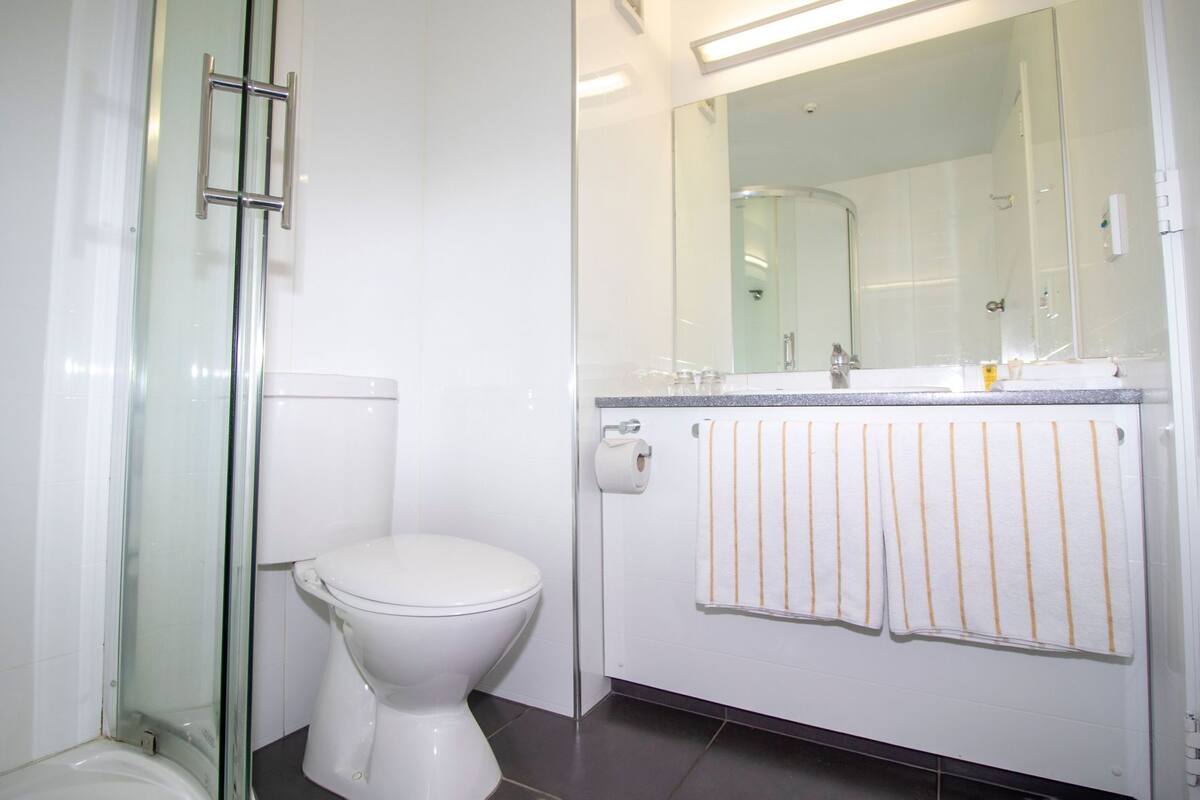 Een moderne badkamer met een douchecabine van glas, een wit toilet en een wastafel met een handdoekhouder.