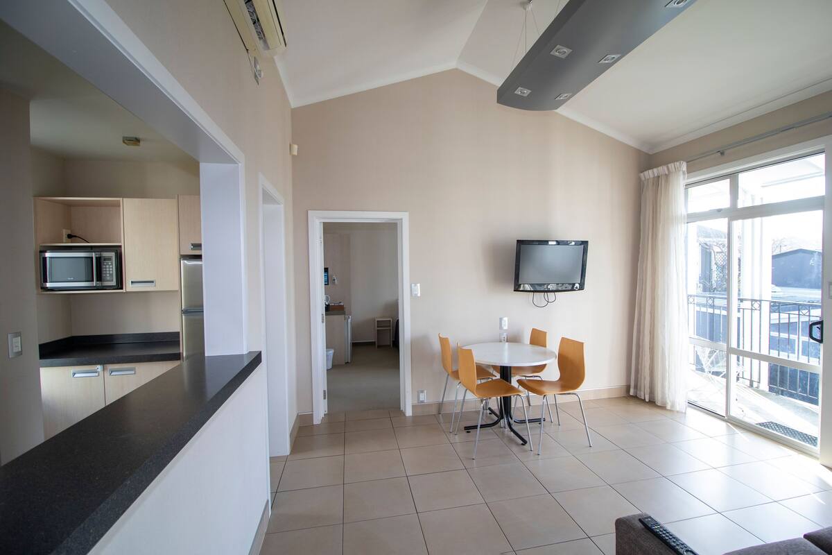 Een moderne keuken met een magnetron en koelkast, een eethoek met een tafel en stoelen, en een groot raam met gordijnen.