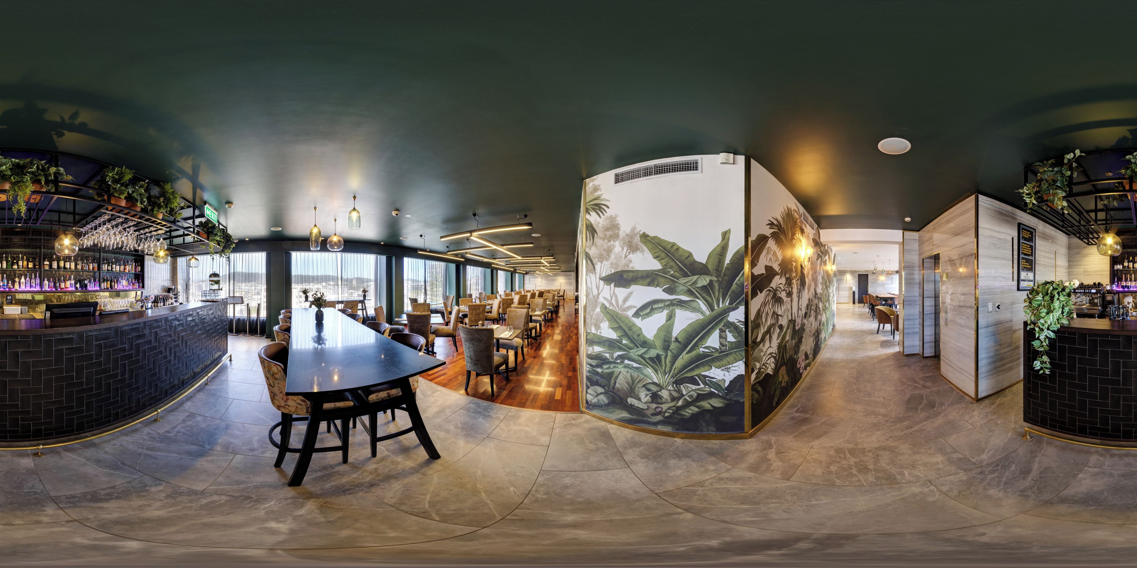 A modern bar area with a curved counter, seating, and a large mural of tropical plants.