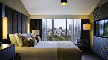Habitación de hotel con una cama grande, dos lámparas de noche, vistas de la ciudad y un candelabro colgante.