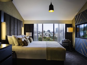 Habitación de hotel con una cama grande, dos lámparas de noche, vistas de la ciudad y un candelabro colgante.
