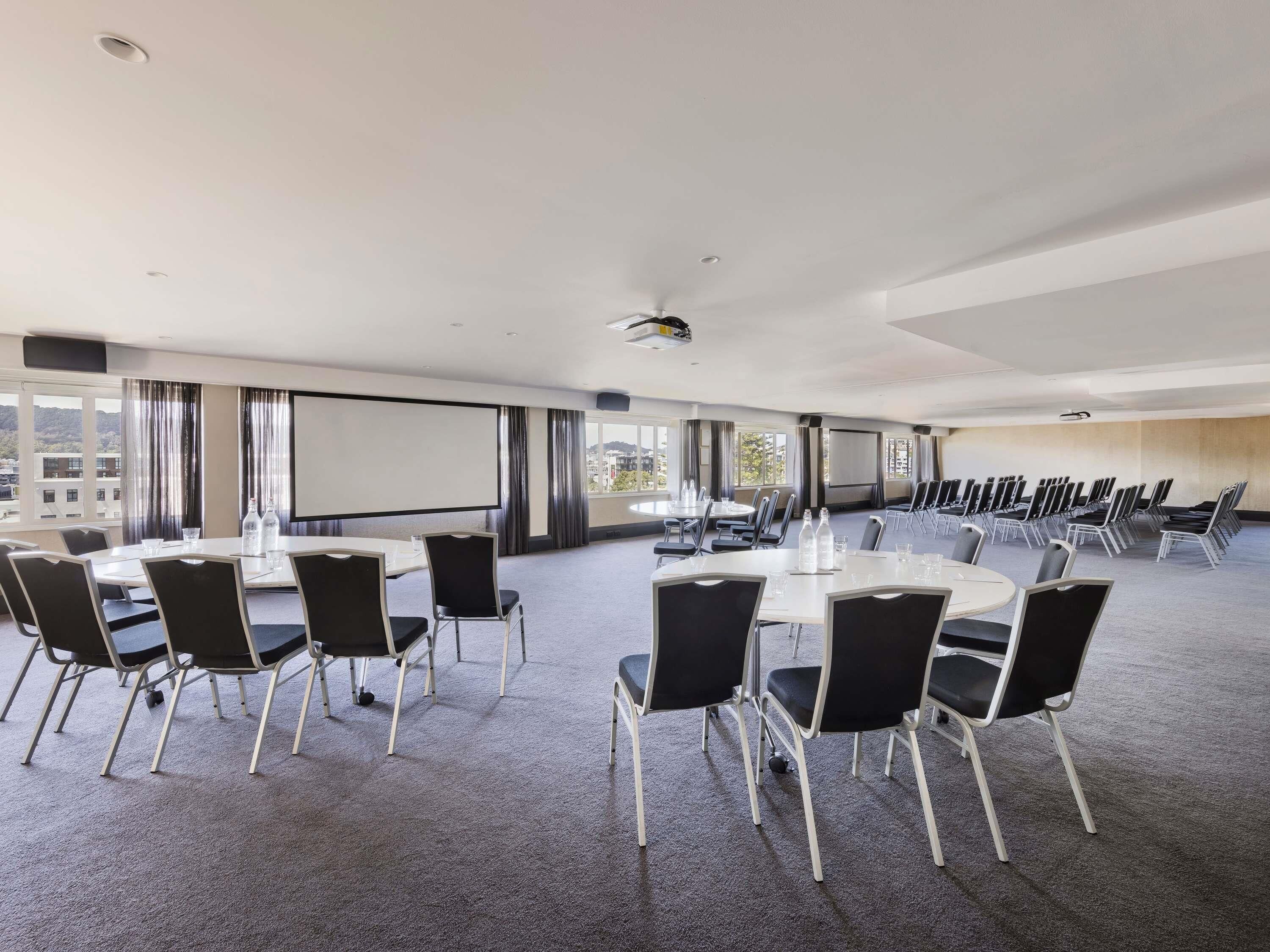Ein Konferenzraum mit großem Tisch, Stühlen, einer Projektionsleinwand und Blick ins Freie.
