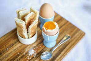 A wooden board with a white cup containing a halved boiled egg, a spoon, and a stack of white breadsticks. - Mövenpick Hotel Wellington (Wellington)