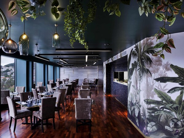 A restaurant with wooden flooring, tables set for dining, hanging plants, and a mural of tropical foliage. - Mövenpick Hotel Wellington (Wellington)