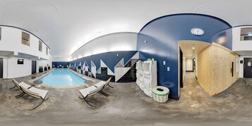 A modern indoor pool area with a blue and white color scheme, a clock on the wall, and a wooden sauna door.