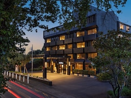 Un hotel moderno con una estructura de varios pisos, una entrada bien iluminada y un camino de entrada arbolado.