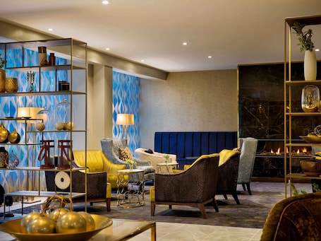 A modern living room with a blue patterned wall, a fireplace, and a yellow sofa.