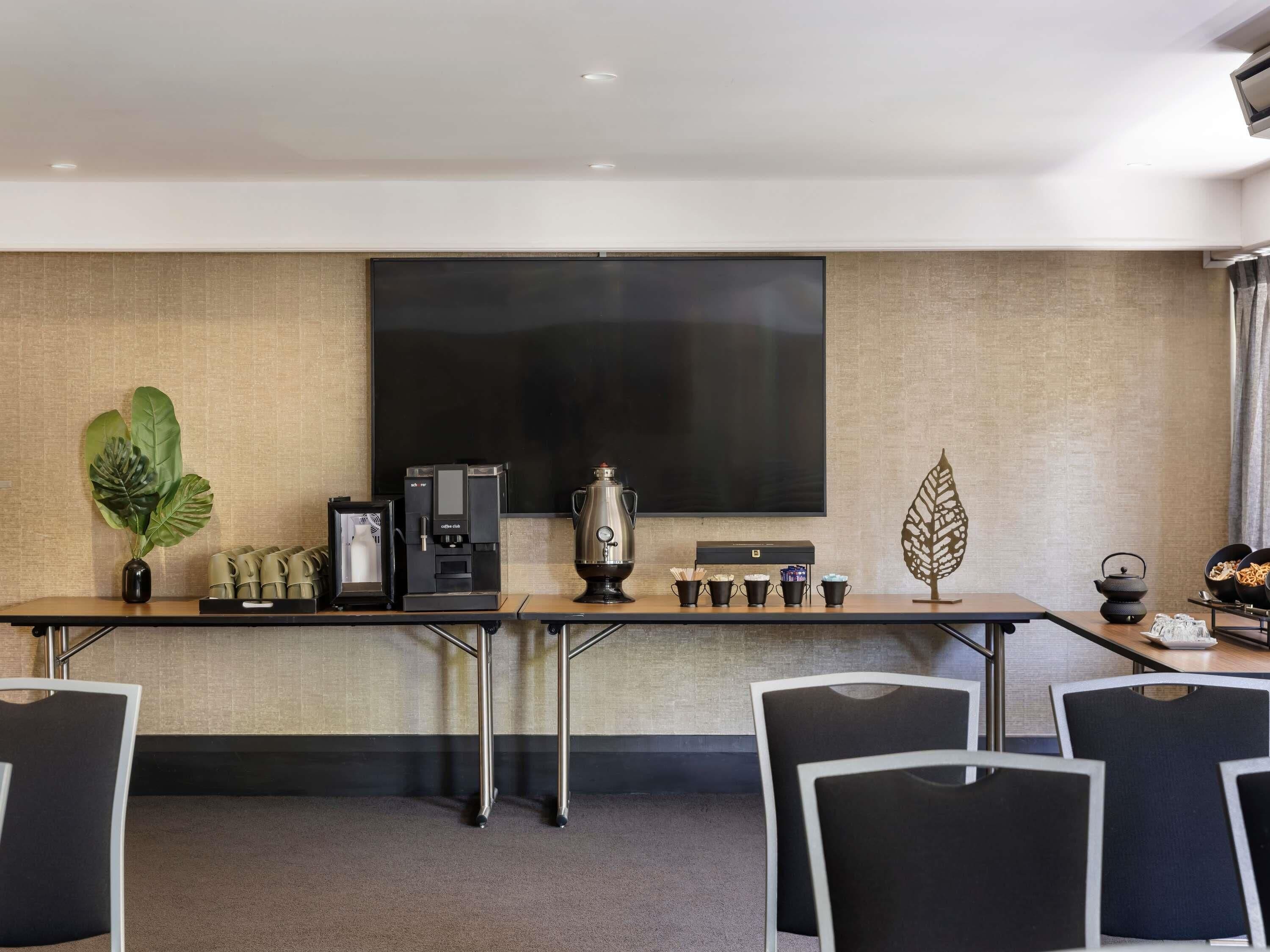 A conference room with a large flat-screen TV, a coffee station, and a decorative plant.