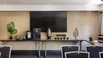 A conference room with a large flat-screen TV, a coffee station, and a decorative plant.