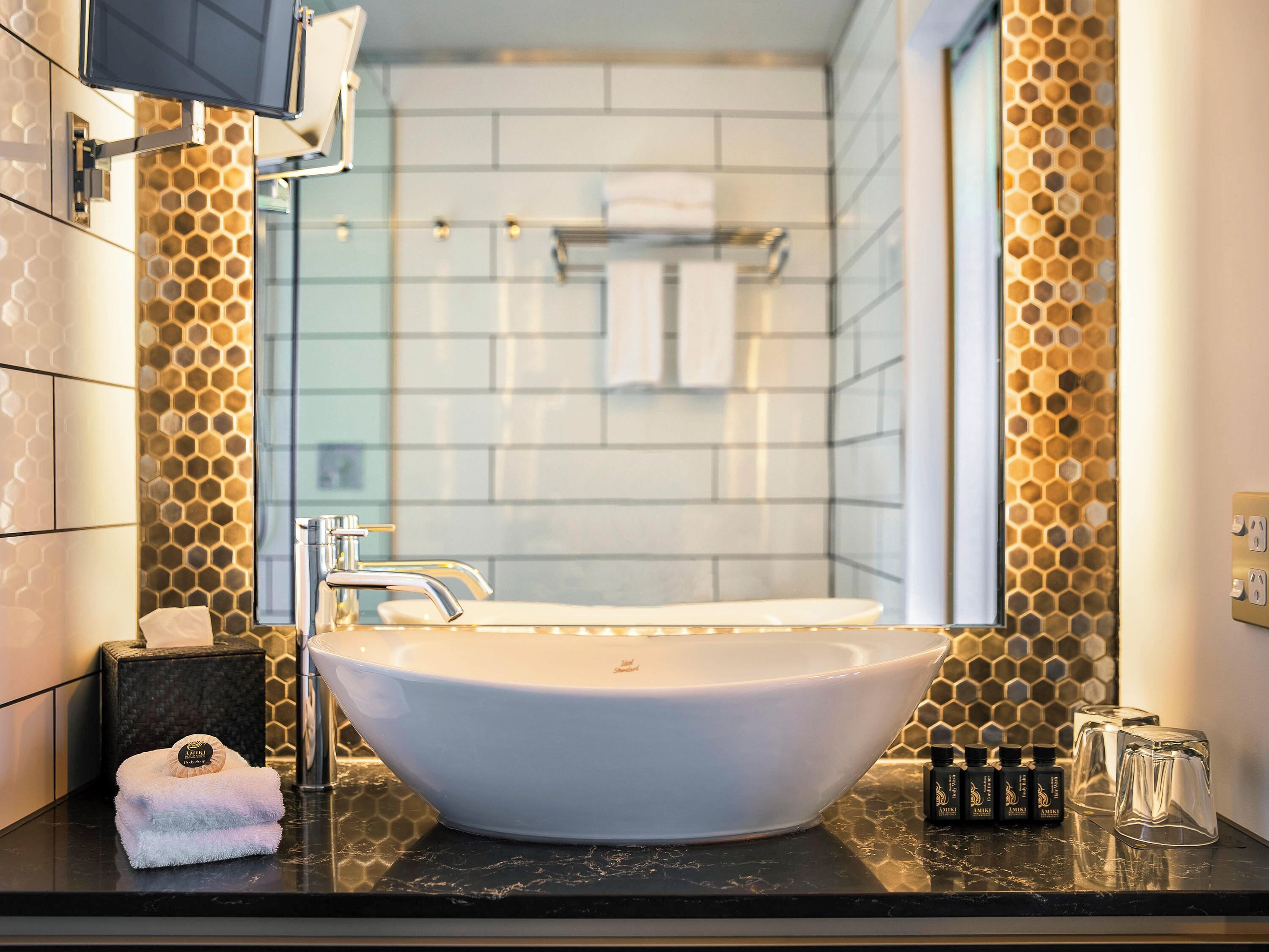 Un baño moderno con un lavabo de diseño, un espejo y un revestimiento mural con patrón de panal.