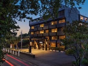 A modern hotel with multiple floors, a well-lit entrance, and a landscaped area with trees. - Mövenpick Hotel Wellington (Wellington)
