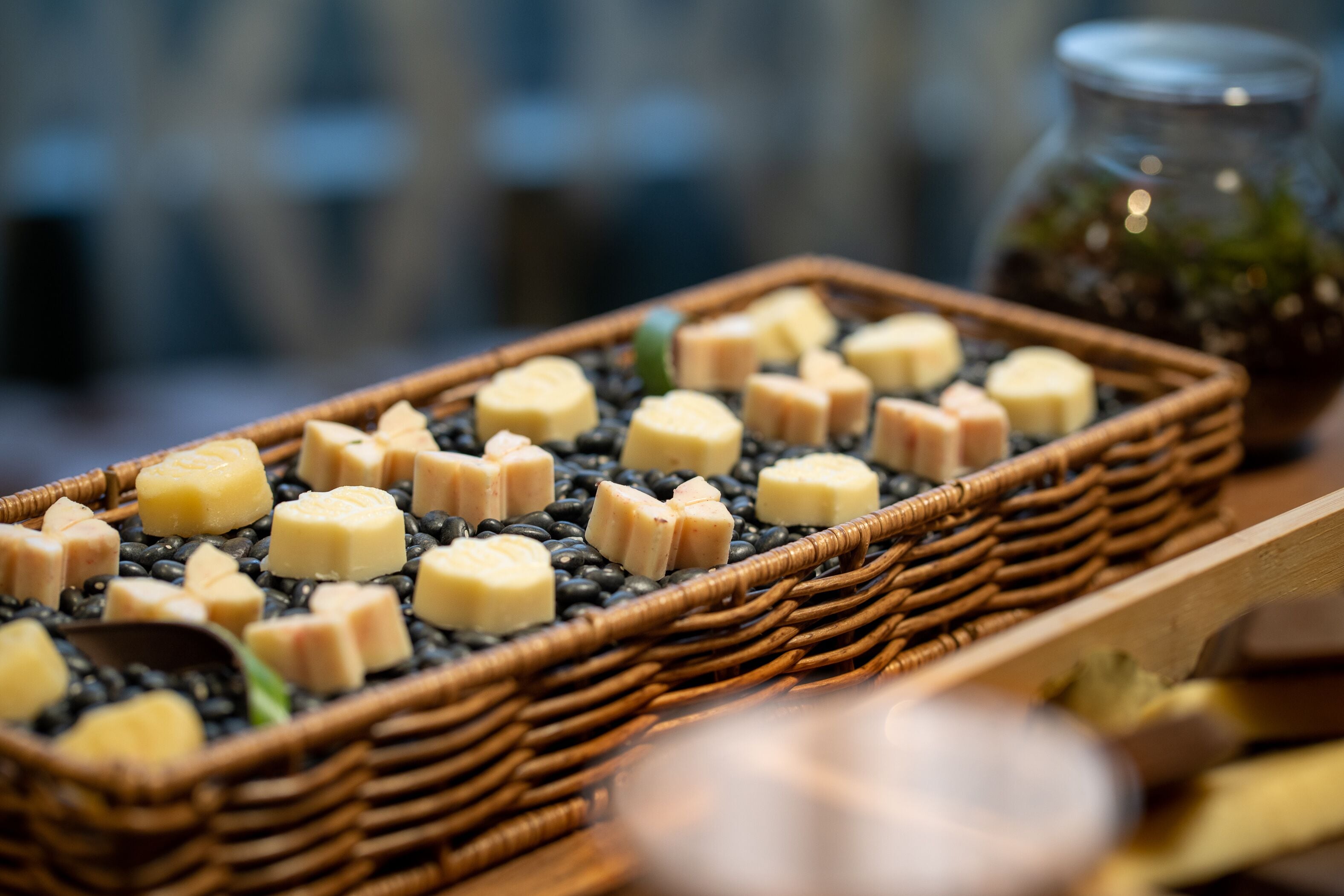 A tray of food items, including cubes of cheese and black beans, on a woven tray.