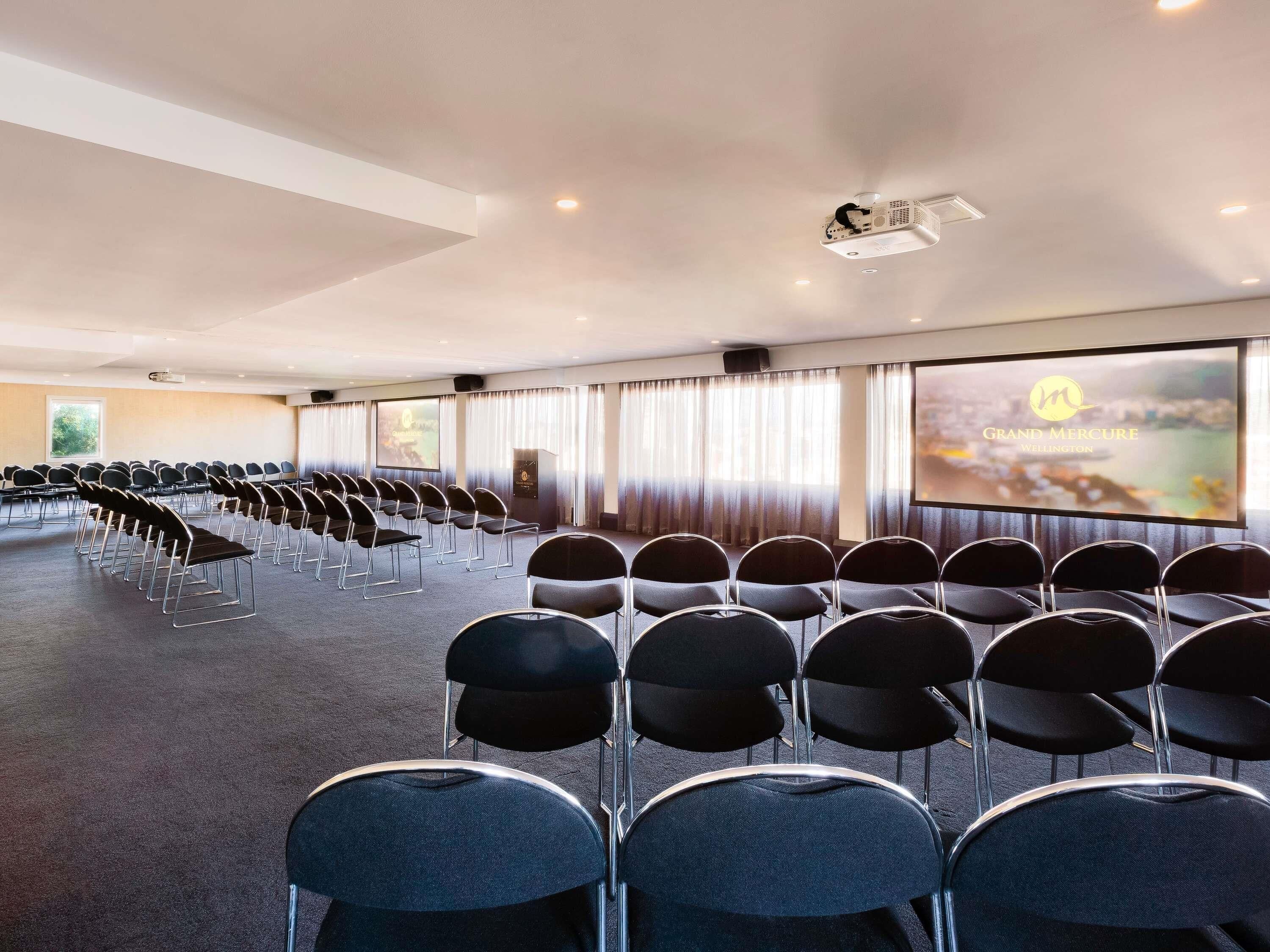 A conference room with rows of chairs, a projection screen, and a speaker system.