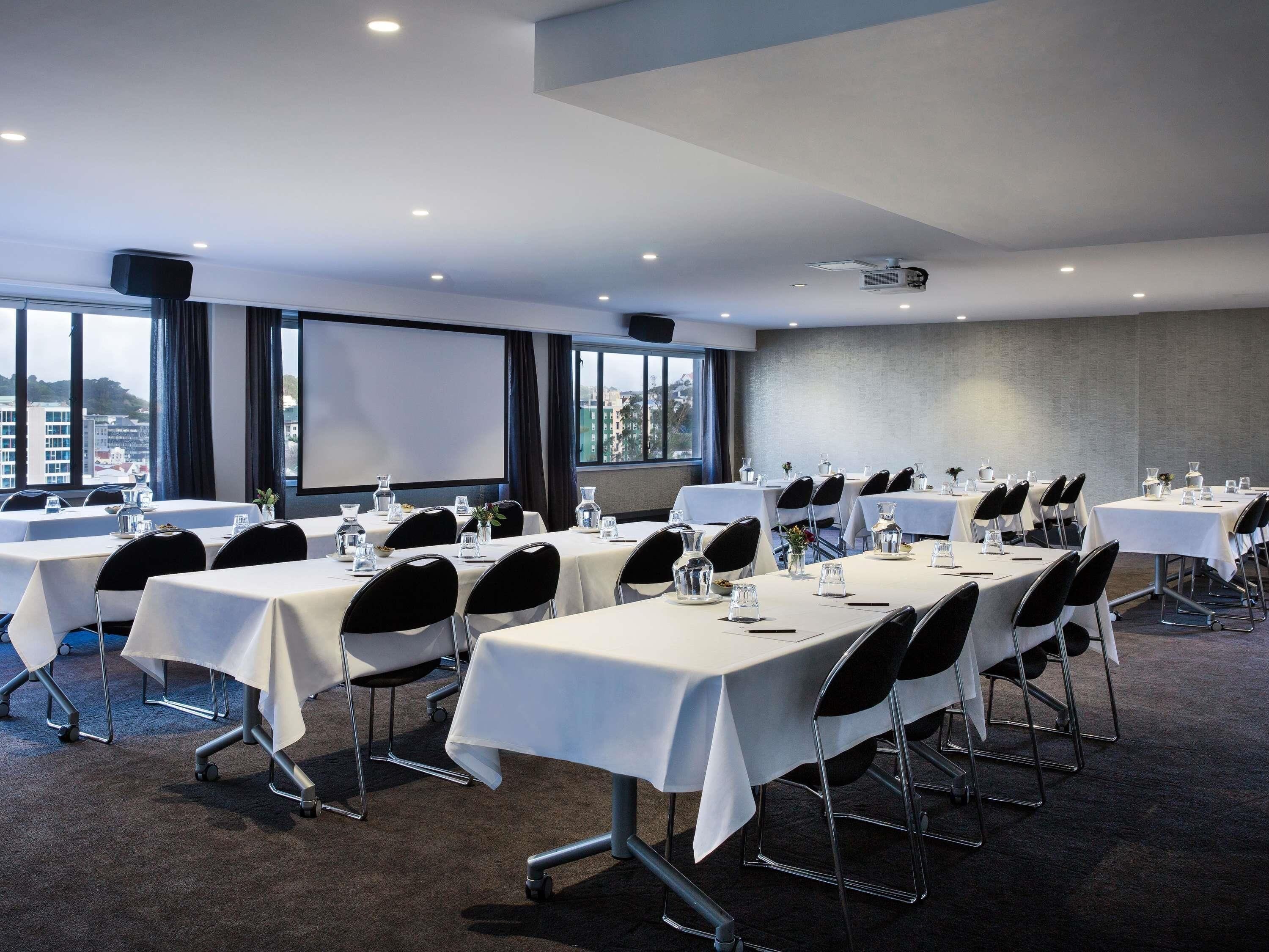 A conference room with tables, chairs, a projector, and a screen.