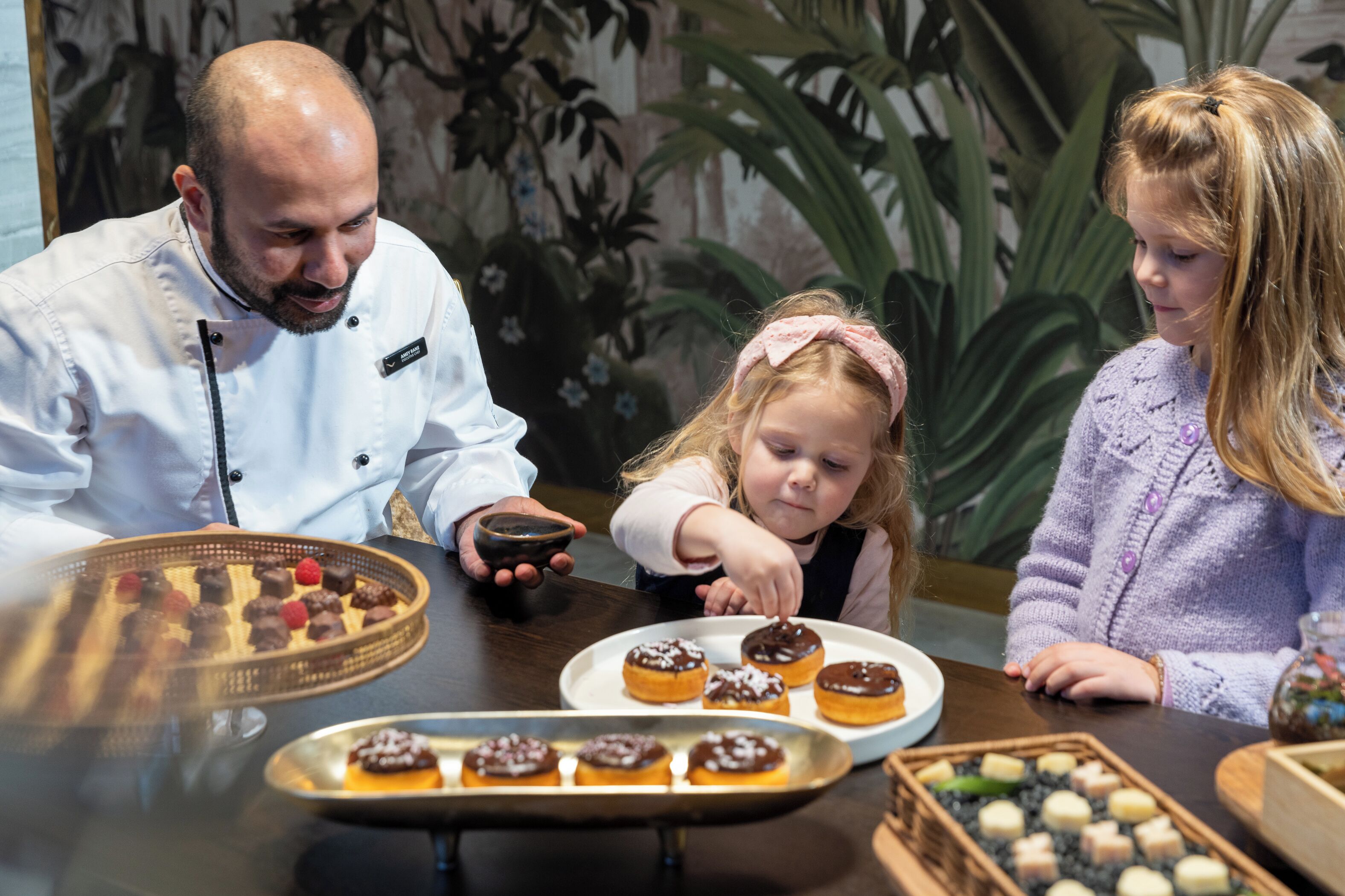 A dining table with various pastries and a chef.