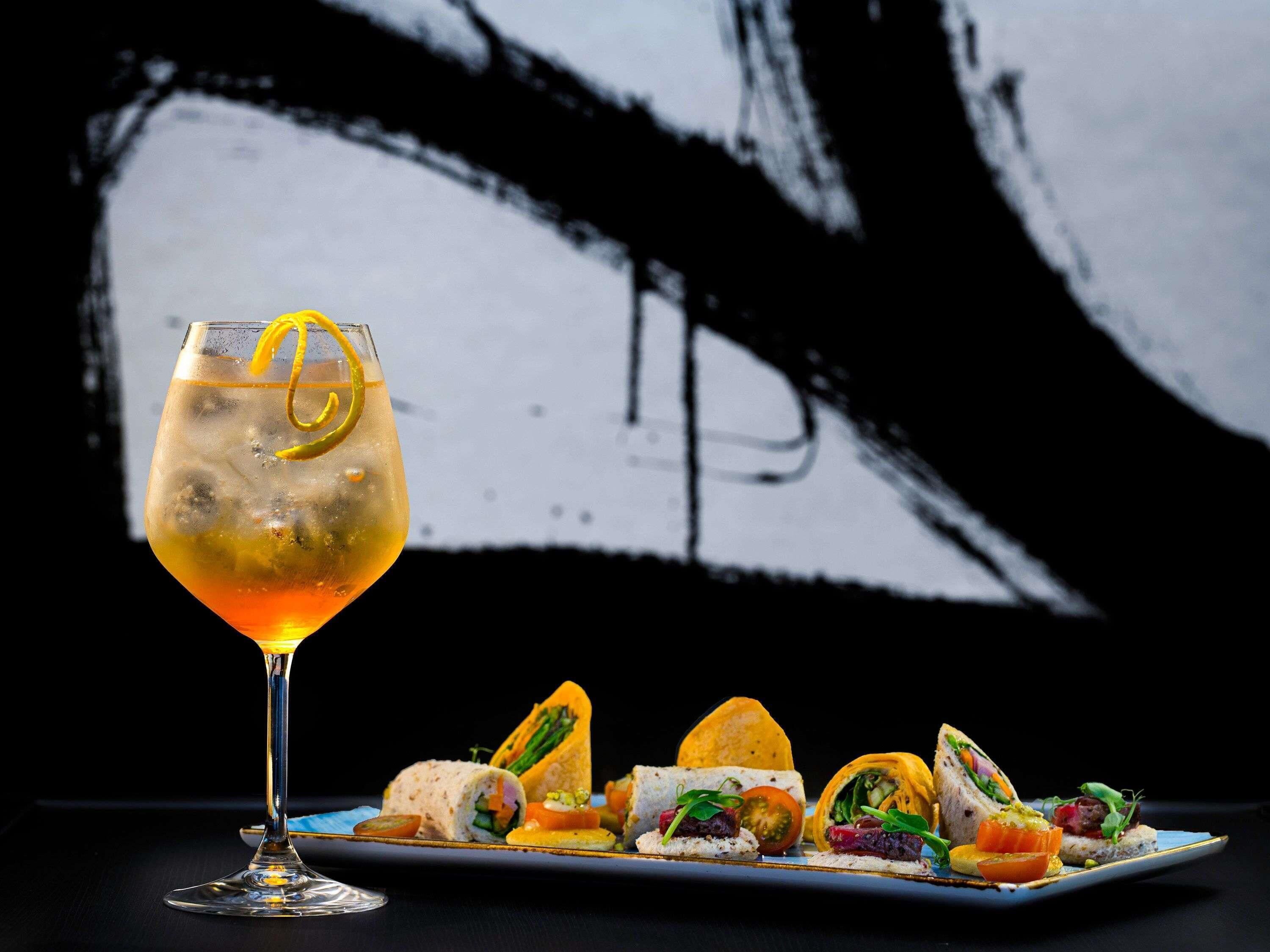 Un cóctel con una rodaja de limón, un plato de aperitivos y un fondo abstracto en blanco y negro.