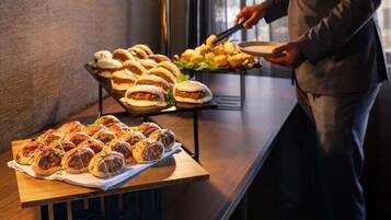 Una mesa de bufé con diversas opciones de comida, incluyendo sándwiches y pasteles, y una persona sirviendo.