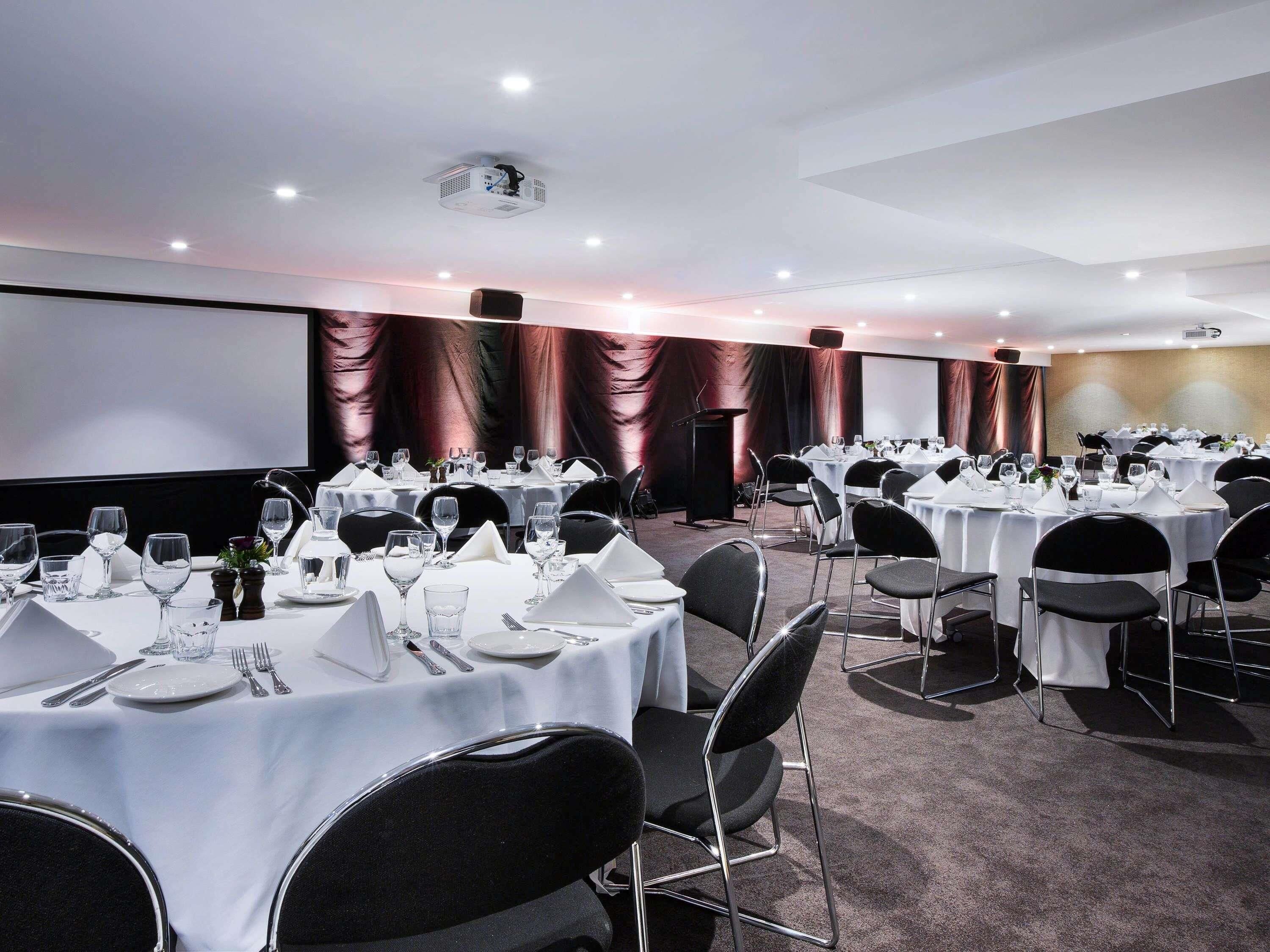 A conference room with round tables, black chairs, and a stage with a podium.
