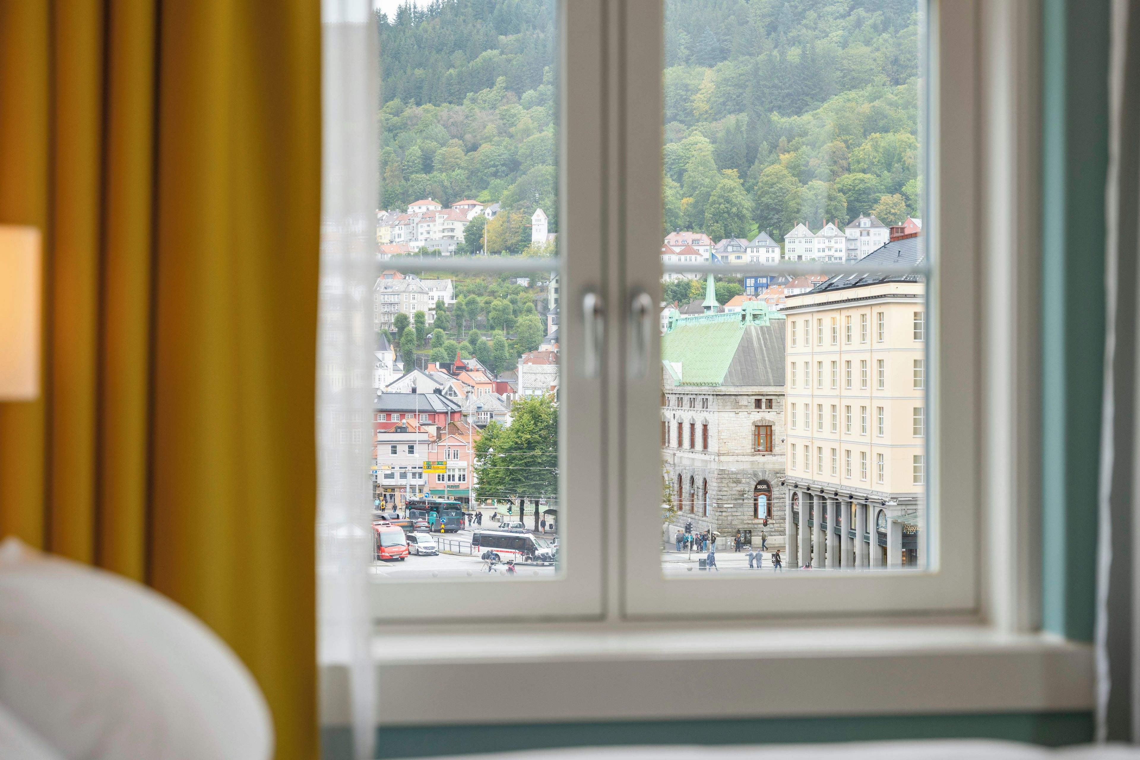Una habitación de hotel con ventana que da a una vista urbana con edificios y una colina verde.