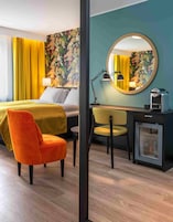 Habitación de hotel con cama, escritorio, silla, espejo y minibar.