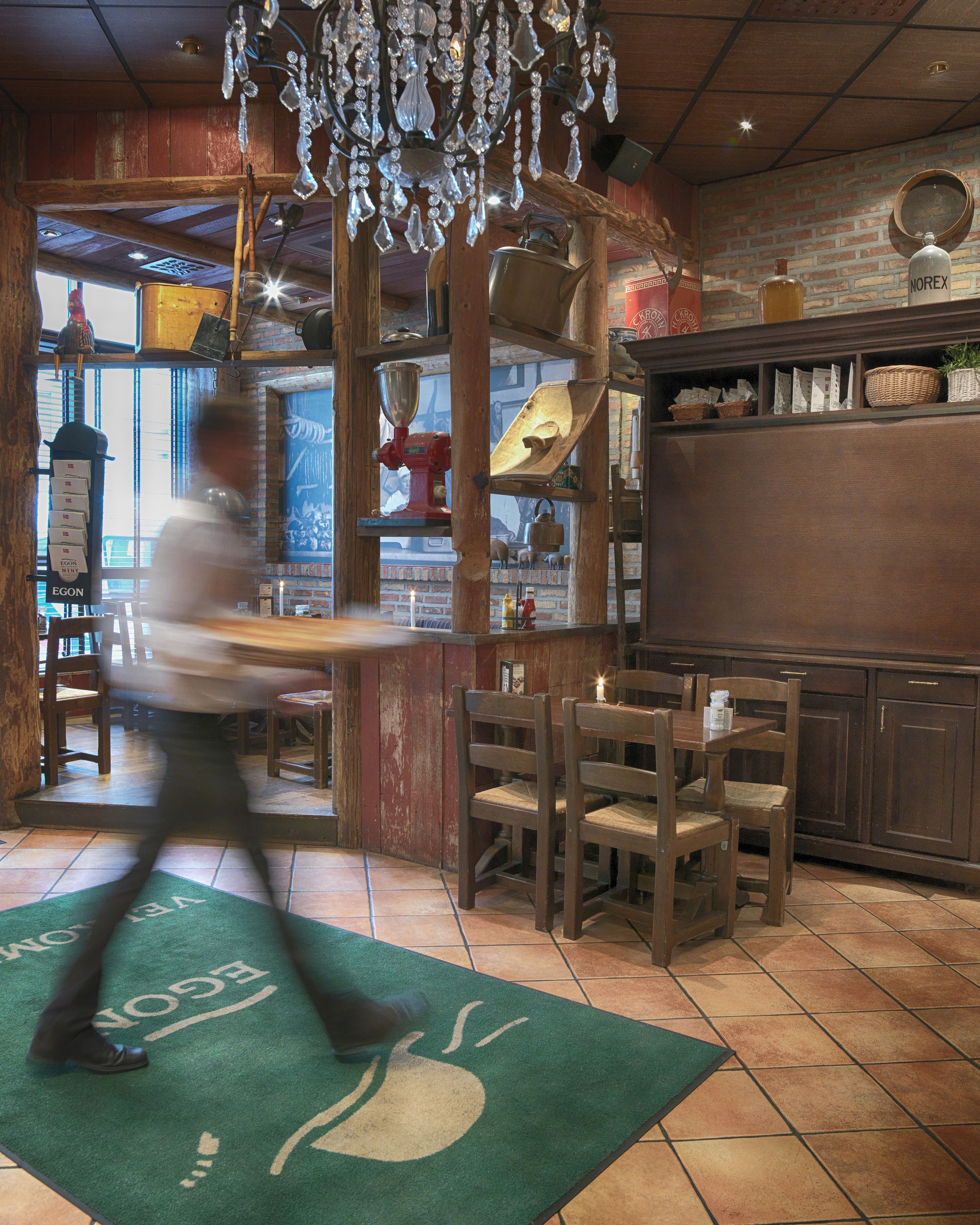 Interior de restaurante con mobiliario de madera, una lámpara de araña y pared de ladrillo.